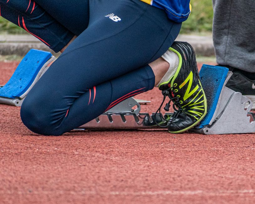 Close-up of a runner's legs ready to start a race, showcasing running shoes and starting block.