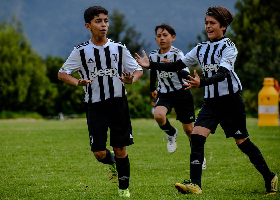 Kids enjoying a game of football outdoors in Juventus jerseys, showcasing teamwork and sportsmanship.