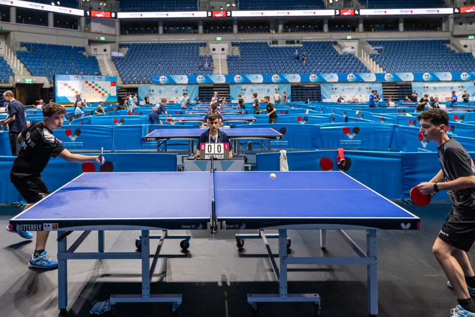 Players compete in a lively table tennis tournament in a large indoor stadium.